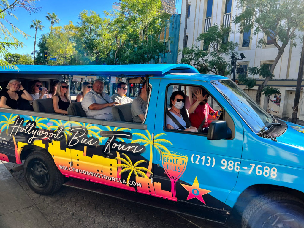 a group of tourists pose for a photo inside of the hollywood bus tours van ready to take the celebrity homes tour of hollywood