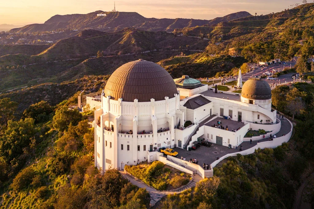 Aerial view of Griffith Observatory with the Los Angeles skyline and Hollywood Hills in the background.