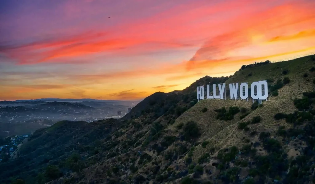 Scenic sunset view of the Hollywood Sign, with warm golden and pink hues lighting up the sky and casting a soft glow over the surrounding hills.