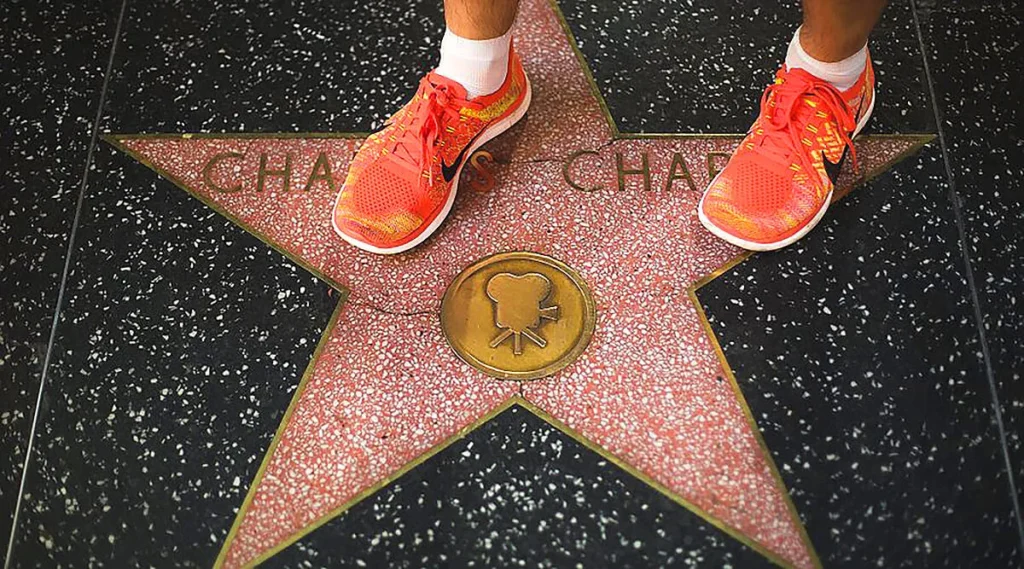 Close-up of a star on the Hollywood Walk of Fame with a person's feet in shoes stepping on it, highlighting the textured sidewalk and brass star details.