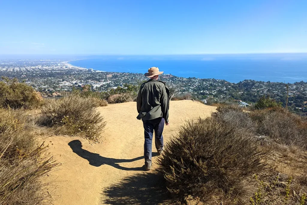 Man standing on a hiking trail at Temescal Canyon with scenic canyon and ocean views in the distance