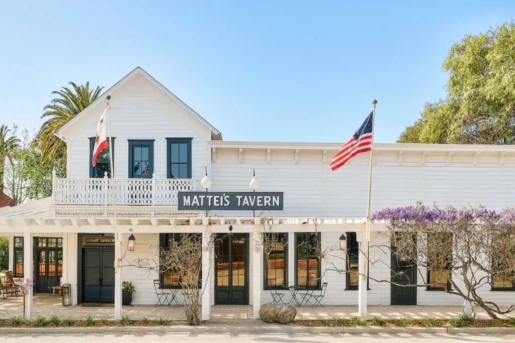 Historic white wooden Mattei's Tavern building with American flag, California state flag, and classic architecture
