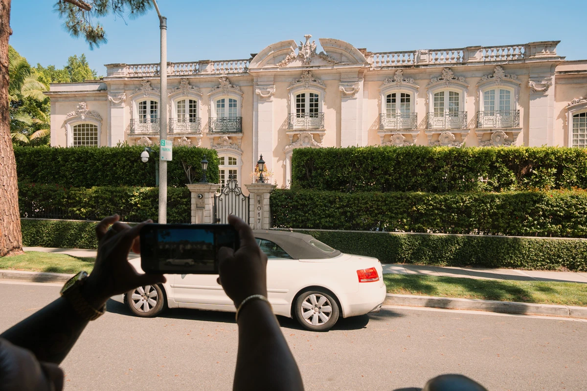 Tourist taking a photo of a luxury mansion during a celebrity homes tour in Beverly Hills.