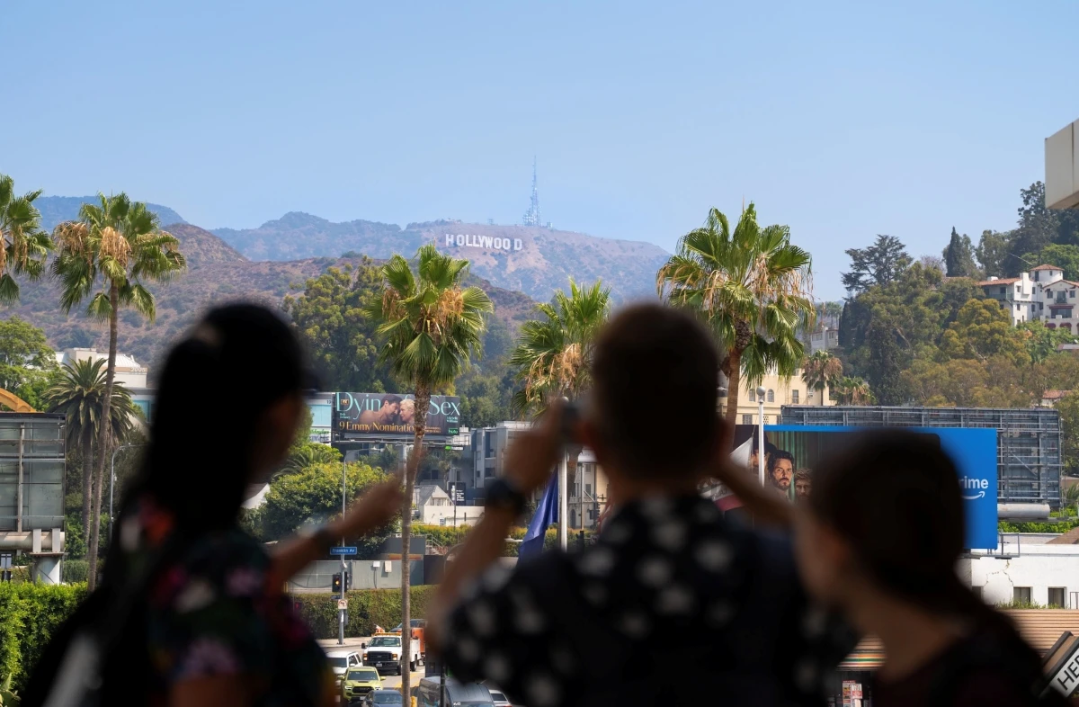 Hollywood sign on hillside with palm trees and tourists in foreground