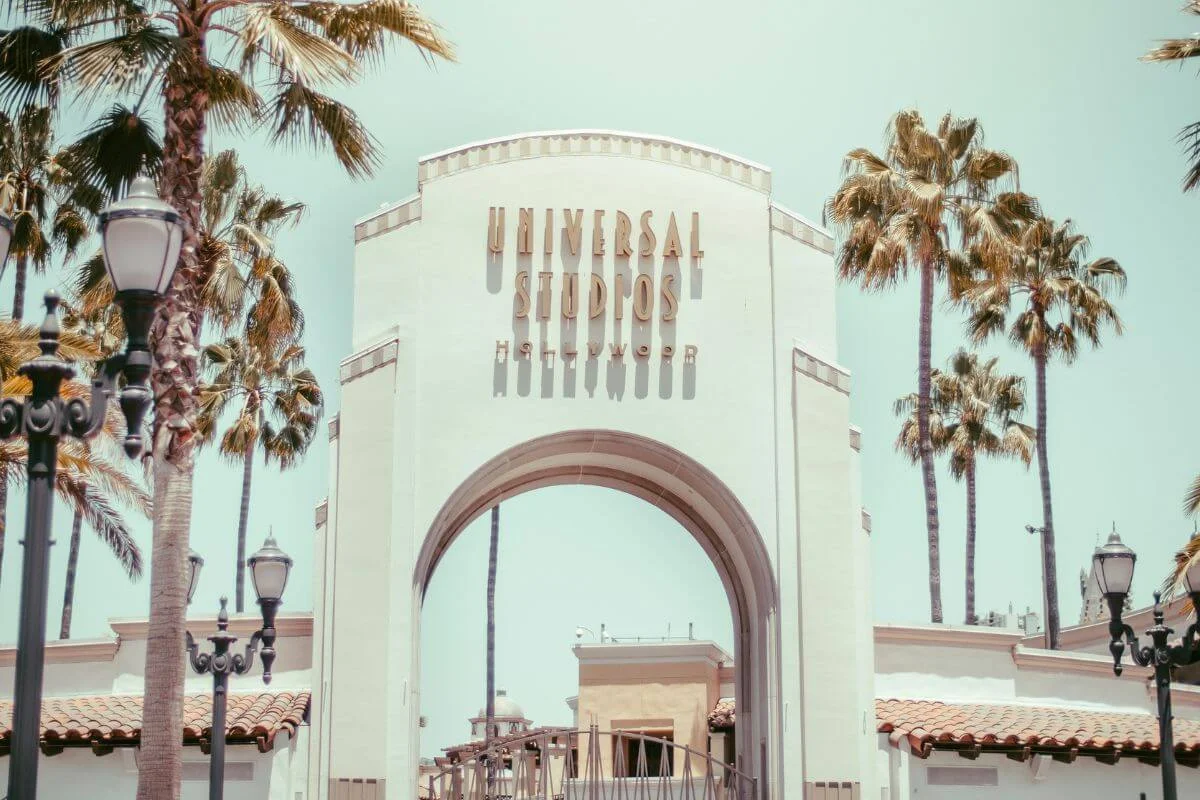 The white arched entrance to Universal Studios Hollywood framed by tall palm trees and decorative street lamps under a bright, clear sky.