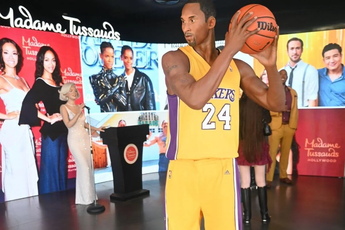 Wax figure of a professional basketball player in a yellow jersey holding a basketball inside Madame Tussauds Hollywood with celebrity displays in the background
