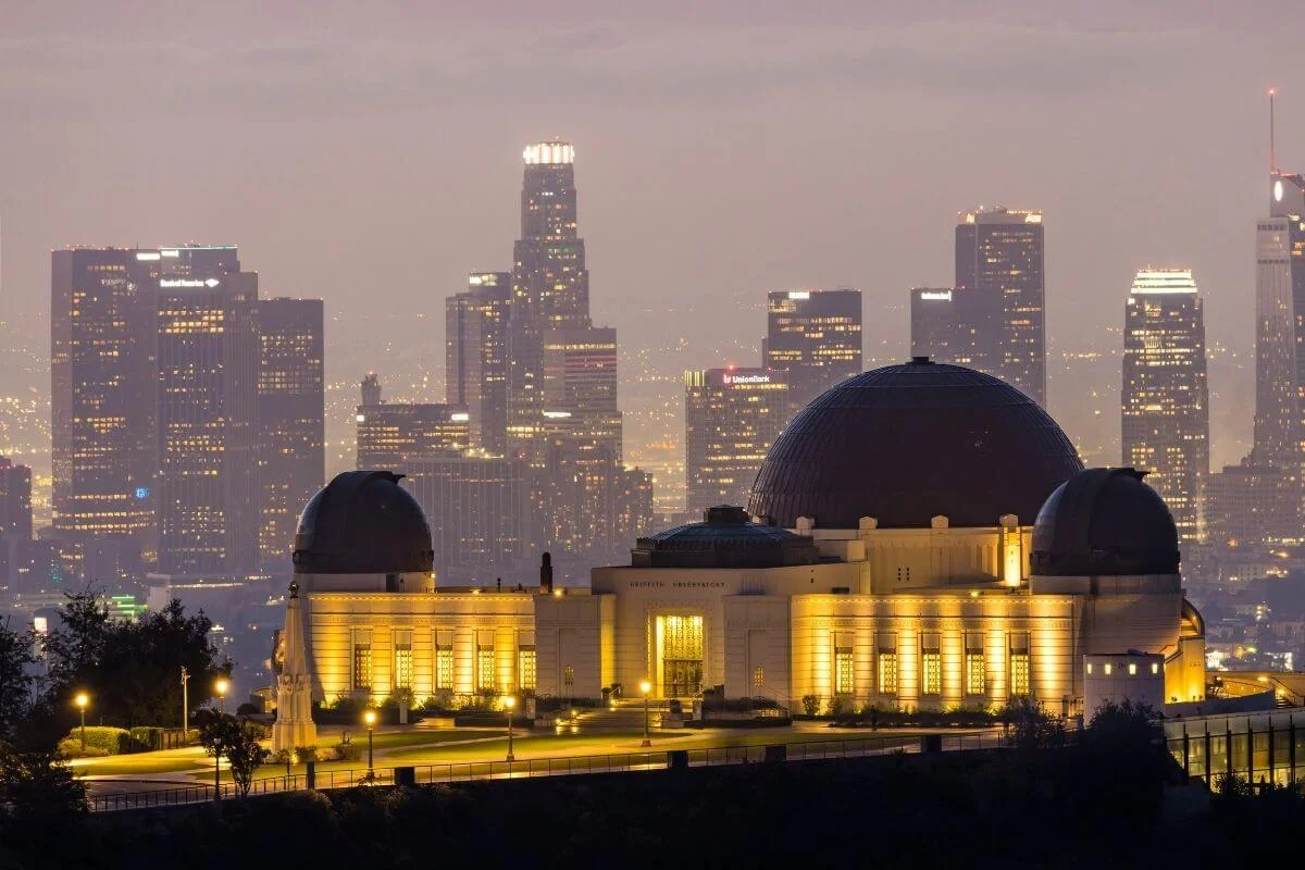 Griffith Observatory illuminated at night with the downtown Los Angeles skyline in the background