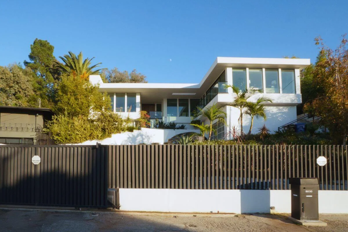 Modern white luxury home with large windows, palm trees, and gated entrance in a residential Beverly Hills neighborhood.