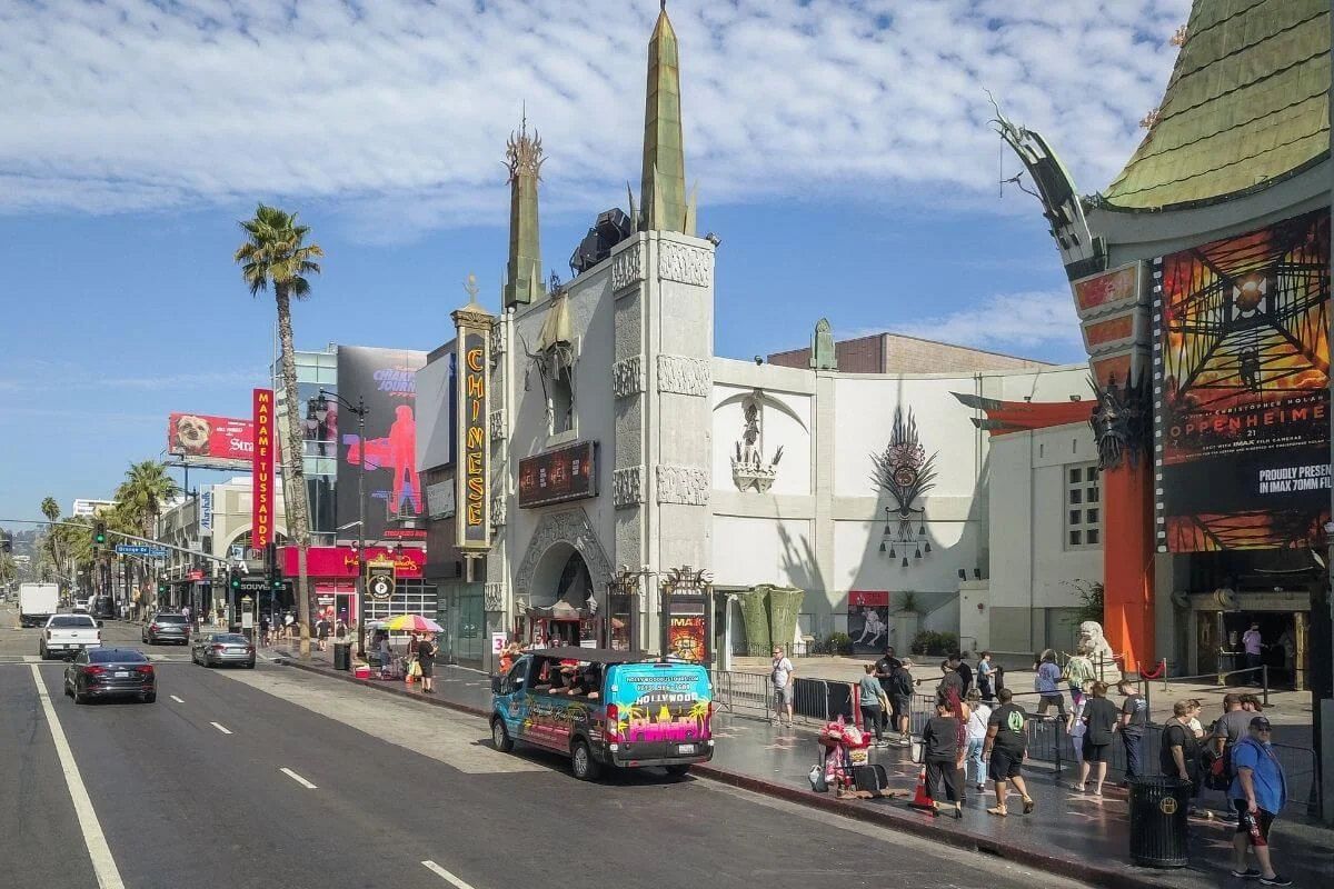 Wide street view of Hollywood Boulevard with the TCL Chinese Theatre, pedestrians, tour vehicles, and nearby attractions
