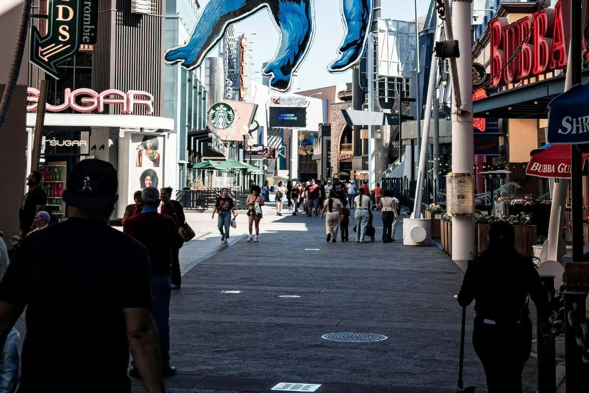 Crowd of visitors walking along the main promenade at Universal CityWalk Hollywood with shops and the King Kong display overhead