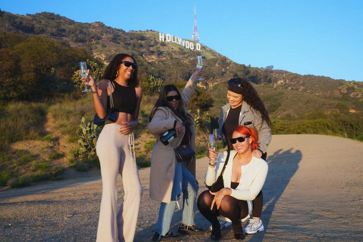 Group of friends toasting with drinks on a hillside with the Hollywood sign in the background