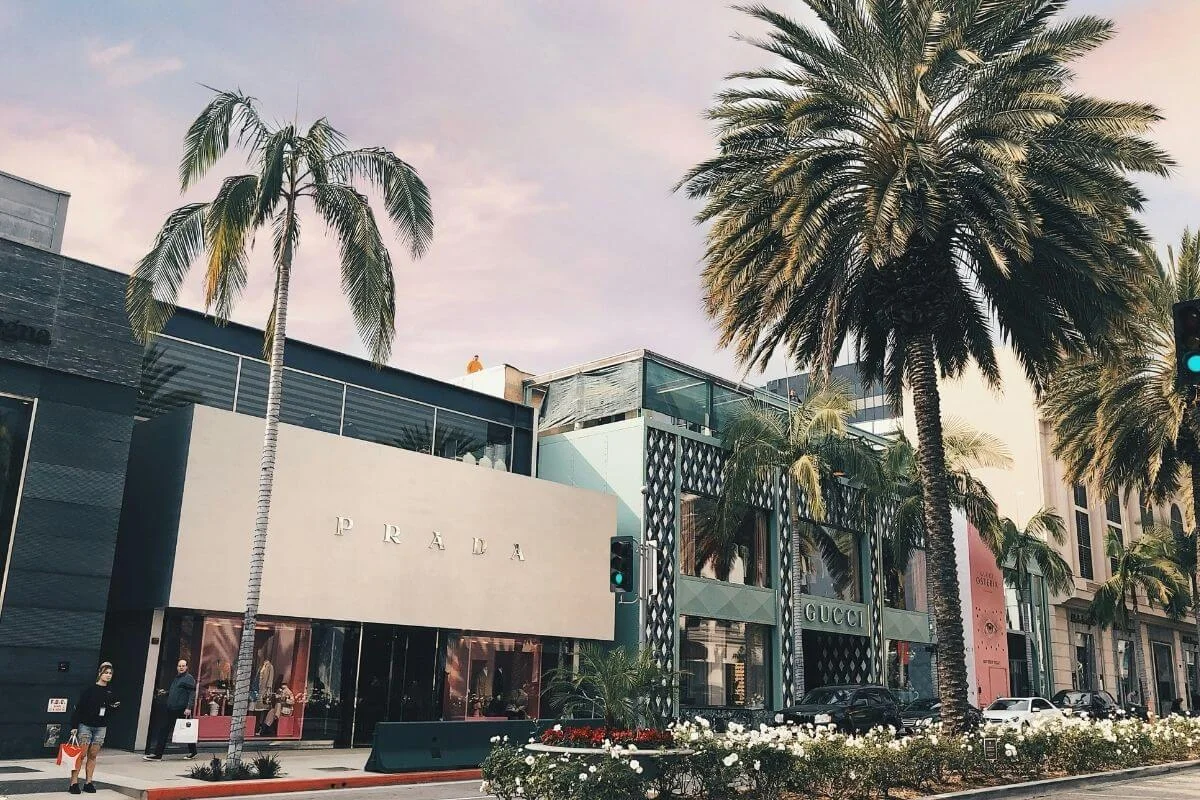 Prada and Gucci storefronts on Rodeo Drive in Beverly Hills with palm trees and pedestrians on a sunny day