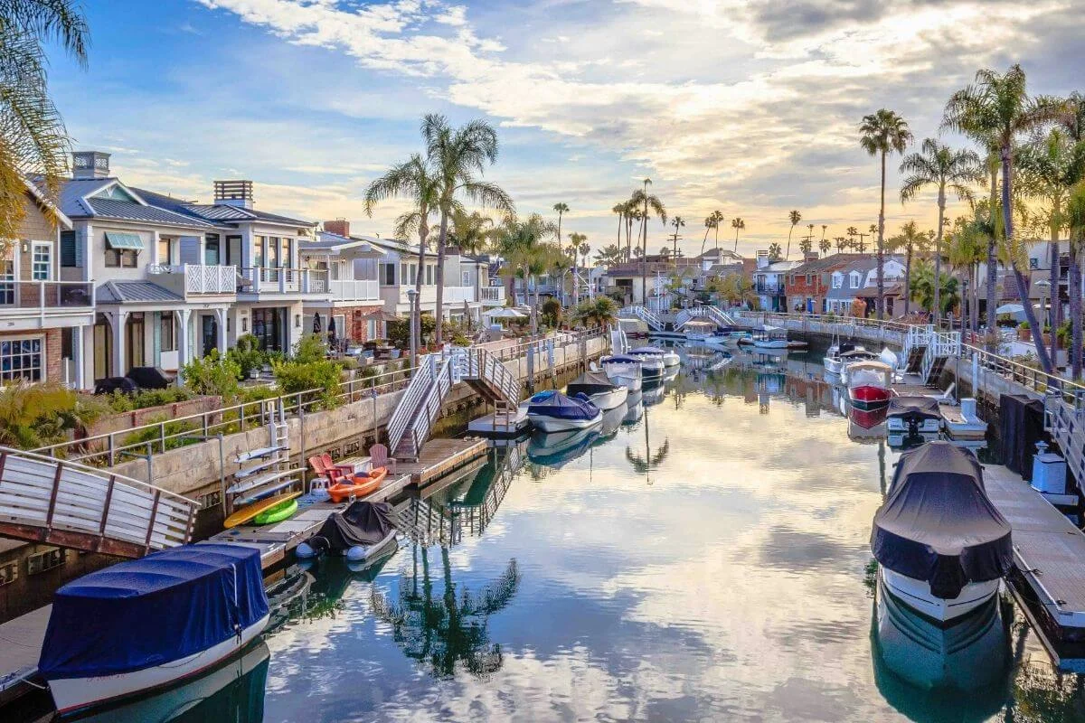 Scenic view of waterfront homes and docked boats along the Naples Canals in Long Beach at sunset with palm trees reflecting on calm water