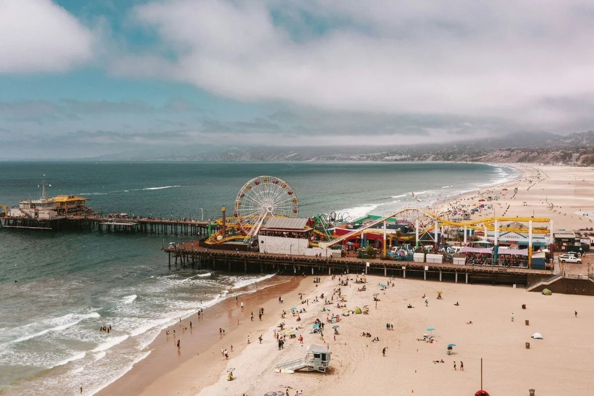 Aerial view of Santa Monica Pier with Ferris wheel and roller coaster overlooking the beach and Pacific Ocean in California.