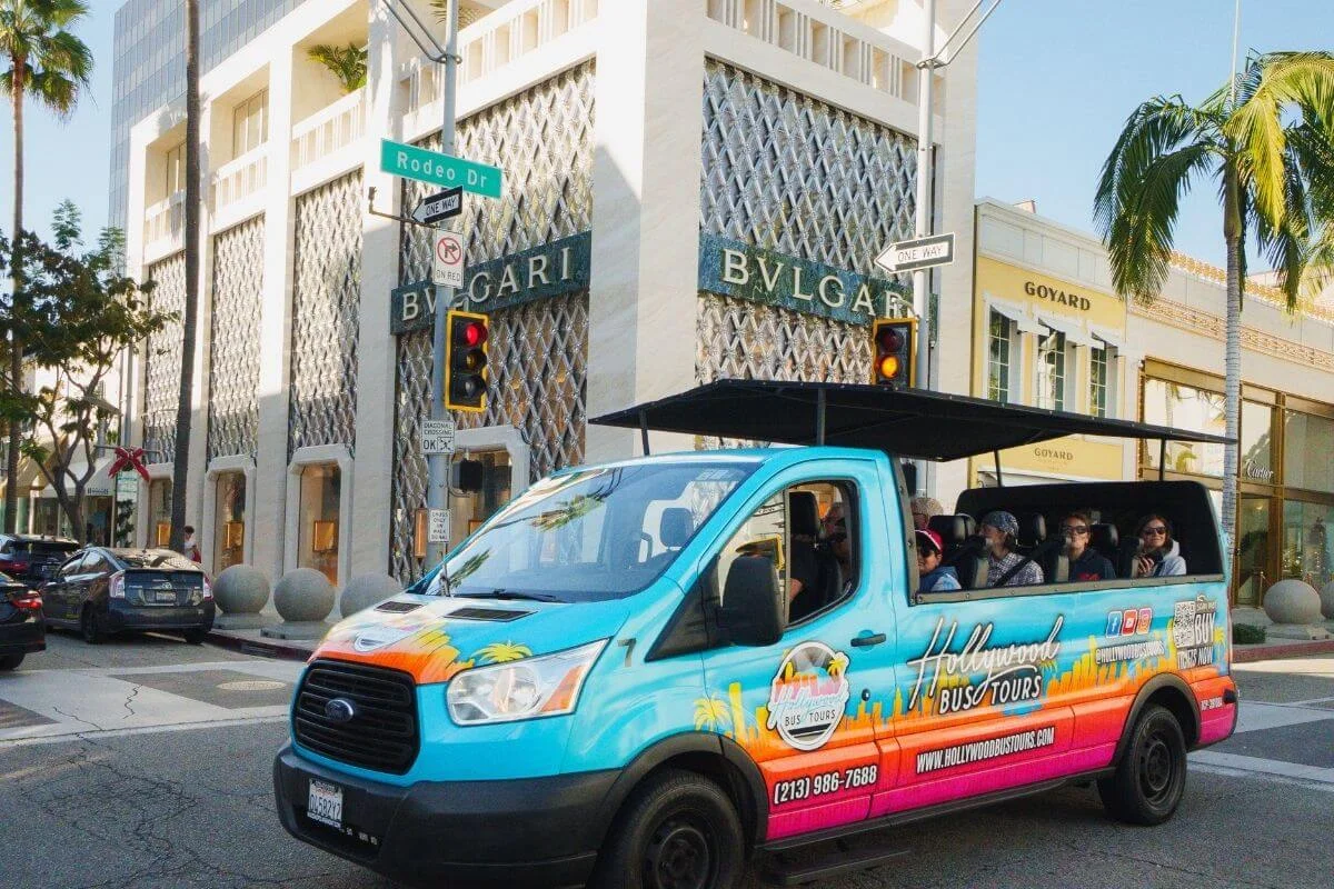 Hollywood Bus Tours open air bus driving past luxury stores on Rodeo Drive in Beverly Hills with passengers onboard