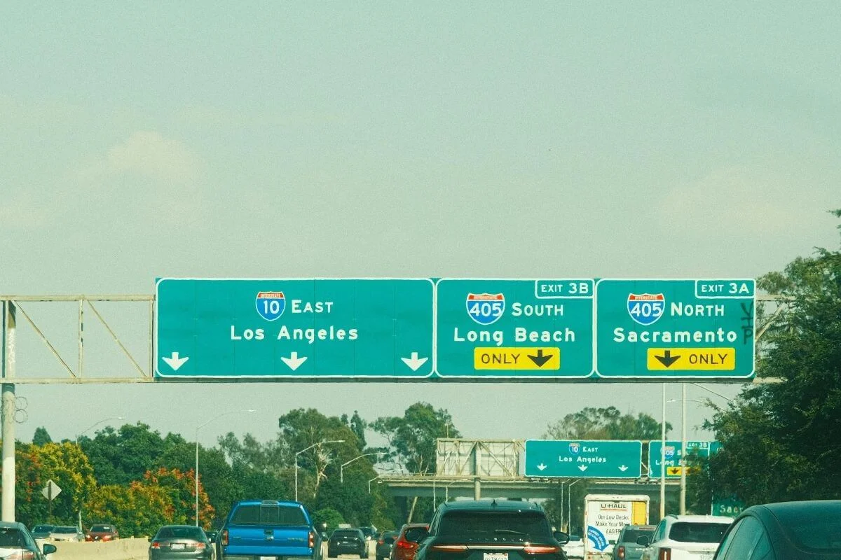 Green freeway signs above traffic showing Interstate 10 East to Los Angeles and Interstate 405 exits toward Long Beach and Sacramento.