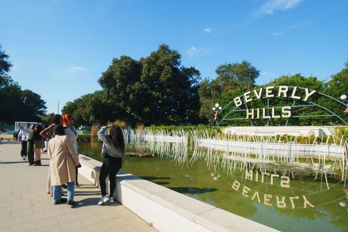 Visitors standing by the Beverly Hills sign and lily pond taking photos during a sightseeing stop in Beverly Hills