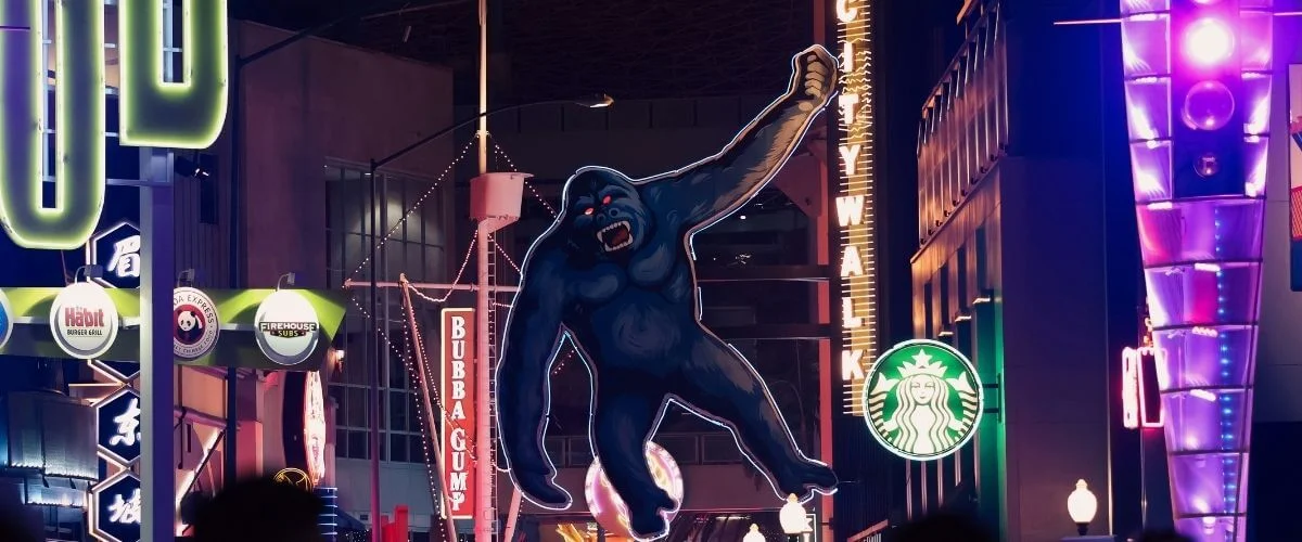 Large illuminated King Kong figure towering above neon signs and storefronts along the Hollywood Walk of Fame at night in Los Angeles.