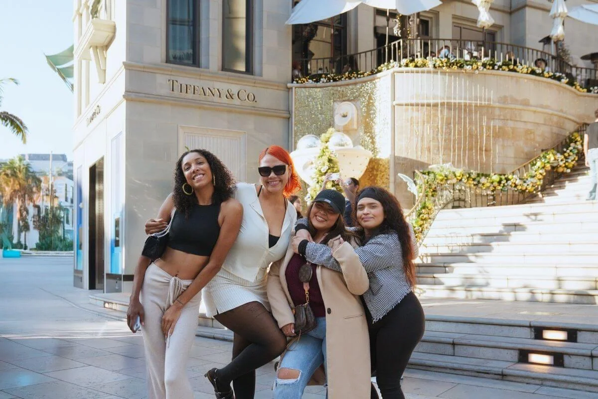 A group of friends posing for a photo outside Tiffany & Co. on Rodeo Drive in Beverly Hills, with elegant storefronts and decorative displays in the background.