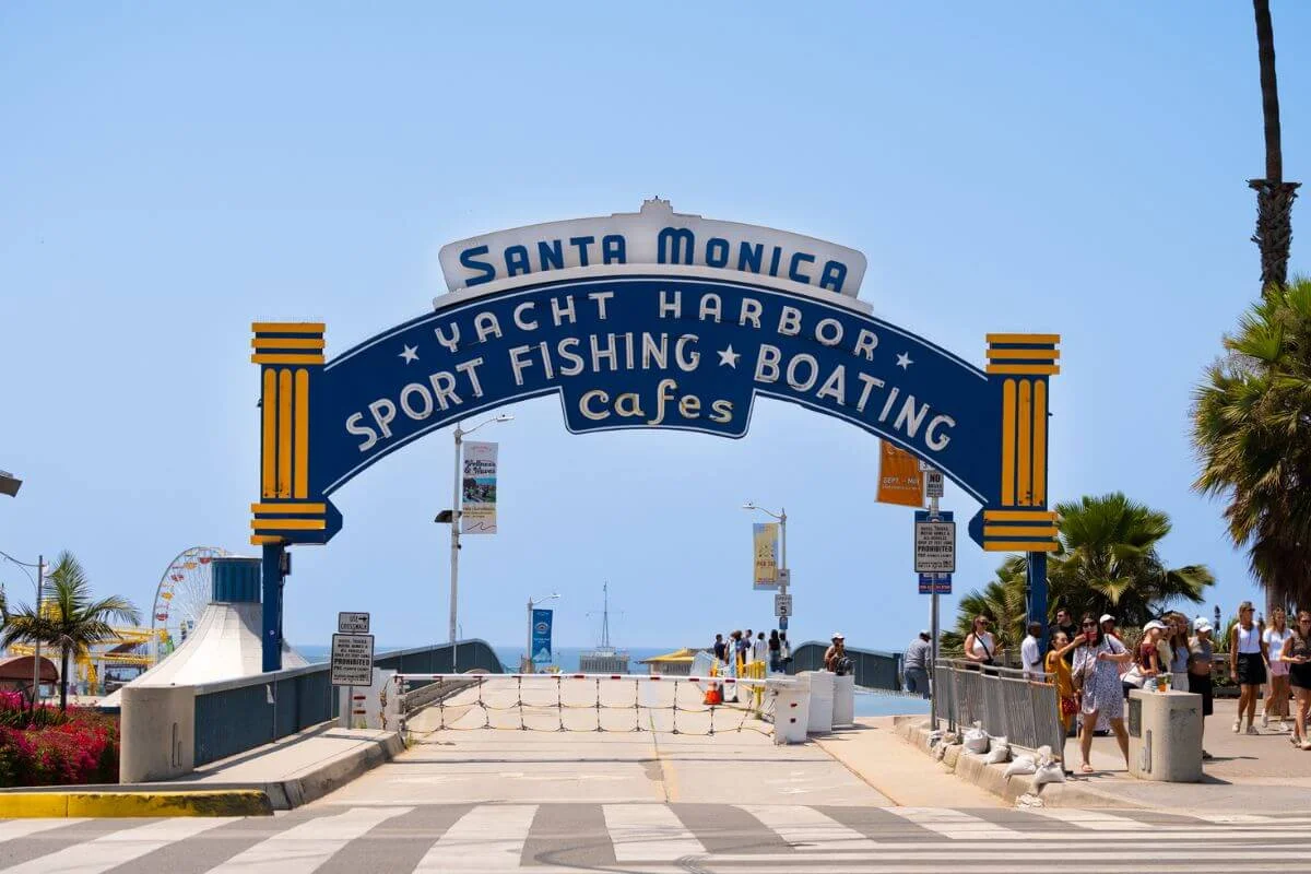 Iconic Santa Monica Yacht Harbor entrance arch at Santa Monica Pier with visitors walking toward the ocean in California.