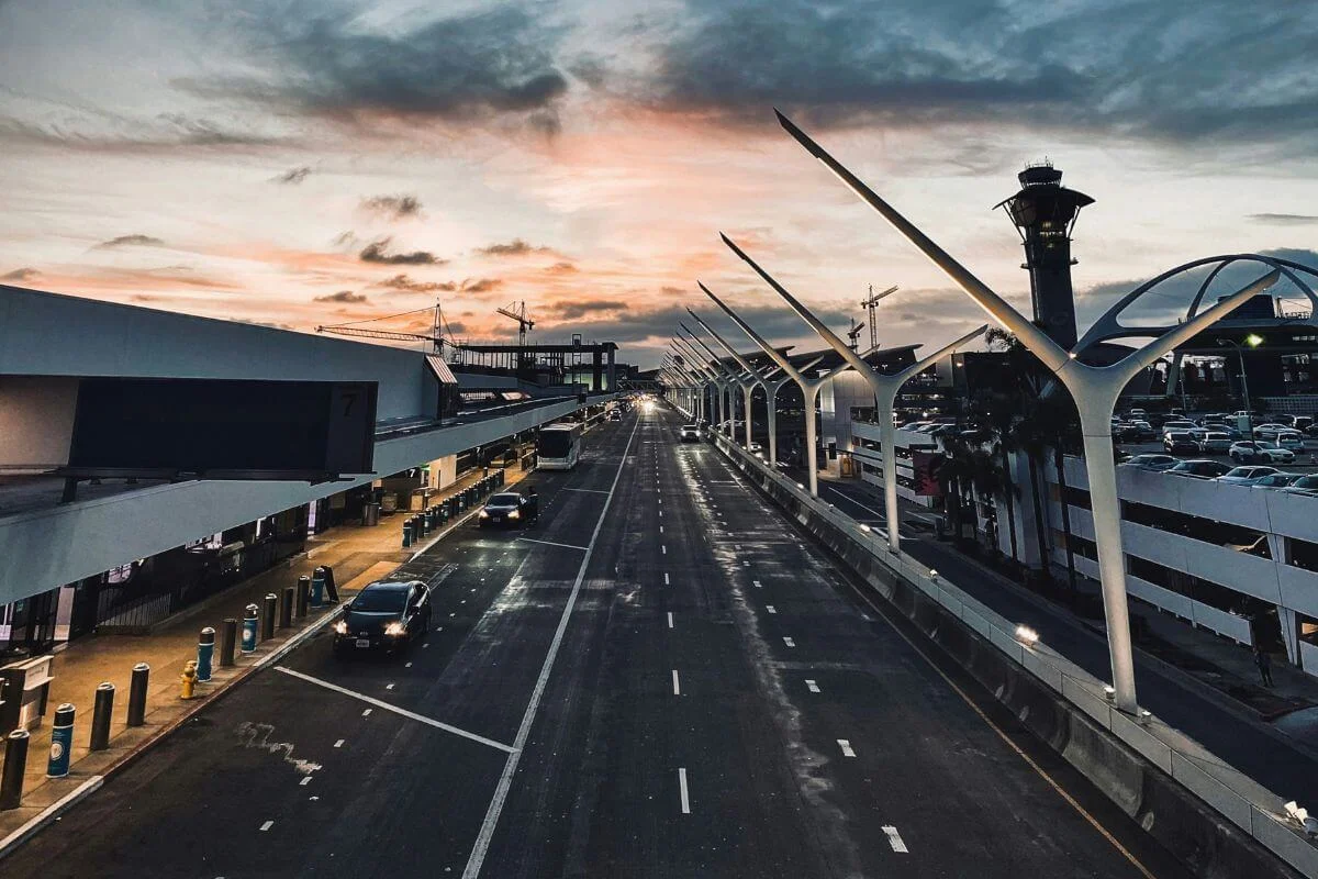 Roadway and terminals at Los Angeles International Airport with the control tower visible during sunset.