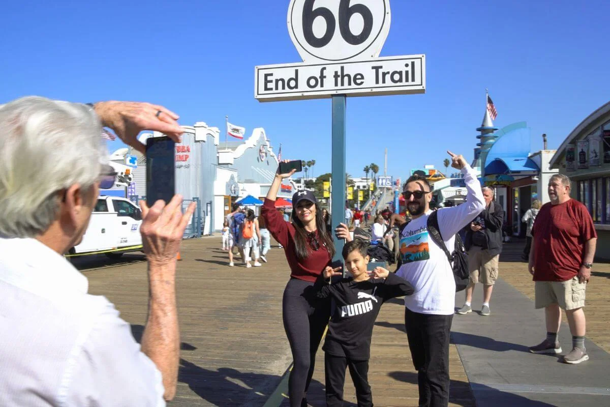 Family posing for a photo under the Route 66 End of the Trail sign at Santa Monica Pier in California.