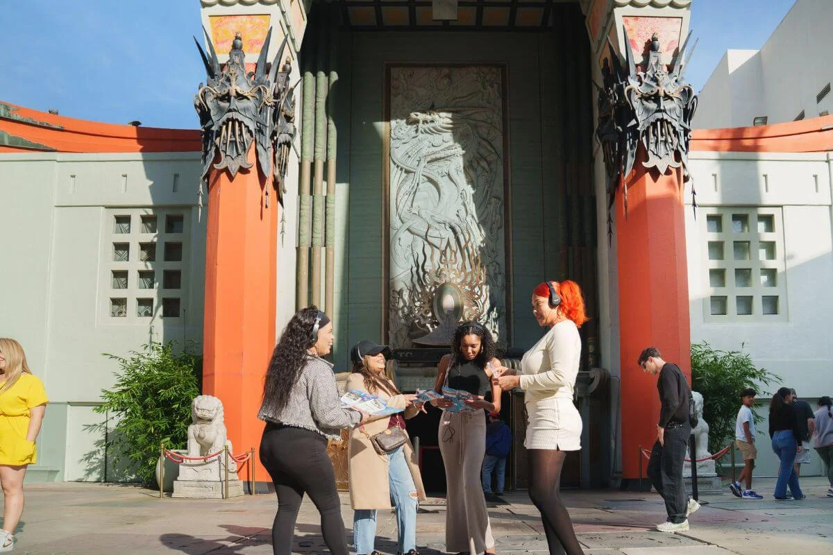 Tourists with headphones reviewing maps outside the entrance of TCL Chinese Theatre on Hollywood Boulevard in Los Angeles.