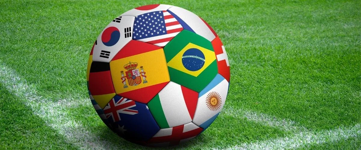 Soccer ball decorated with international country flags resting on a green grass football field.