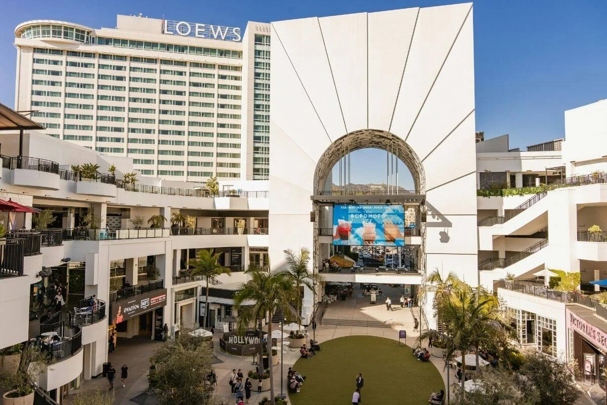 Aerial view of Ovation Hollywood with open-air shopping levels, palm trees, and Loews Hollywood Hotel overlooking the courtyard in Los Angeles.