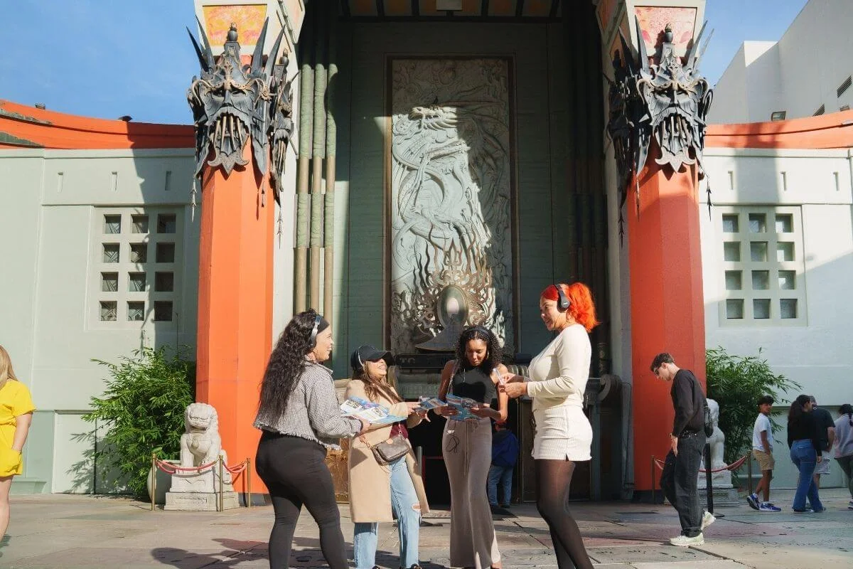 Group of tourists holding maps and listening to audio guides while standing in front of the iconic TCL Chinese Theatre in Hollywood, Los Angeles.