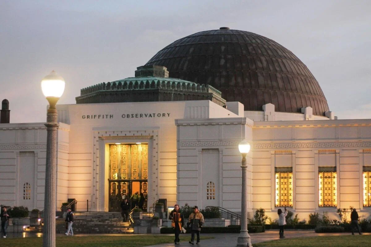 Griffith Observatory illuminated at dusk in Los Angeles, featuring its iconic dome and visitors gathered outside the historic landmark.