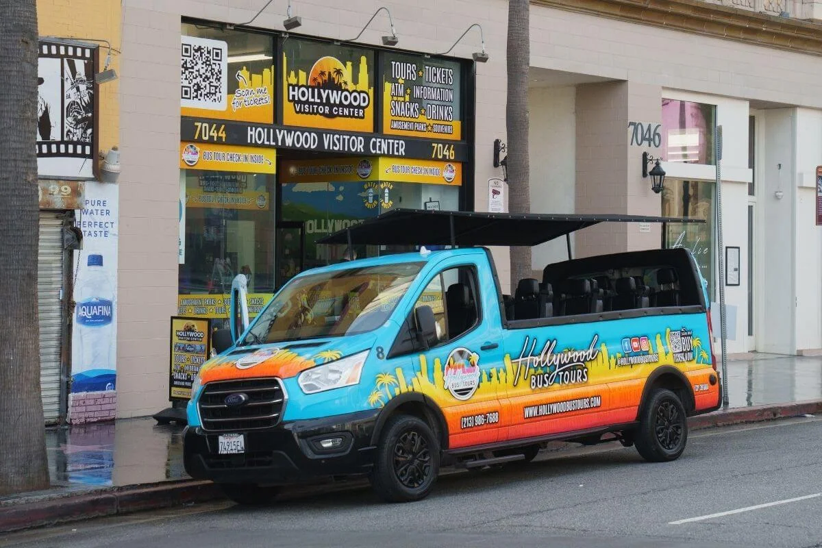 Colorful Hollywood Bus Tours van parked outside the Hollywood Visitor Center on a city street, ready for sightseeing tours in Los Angeles.