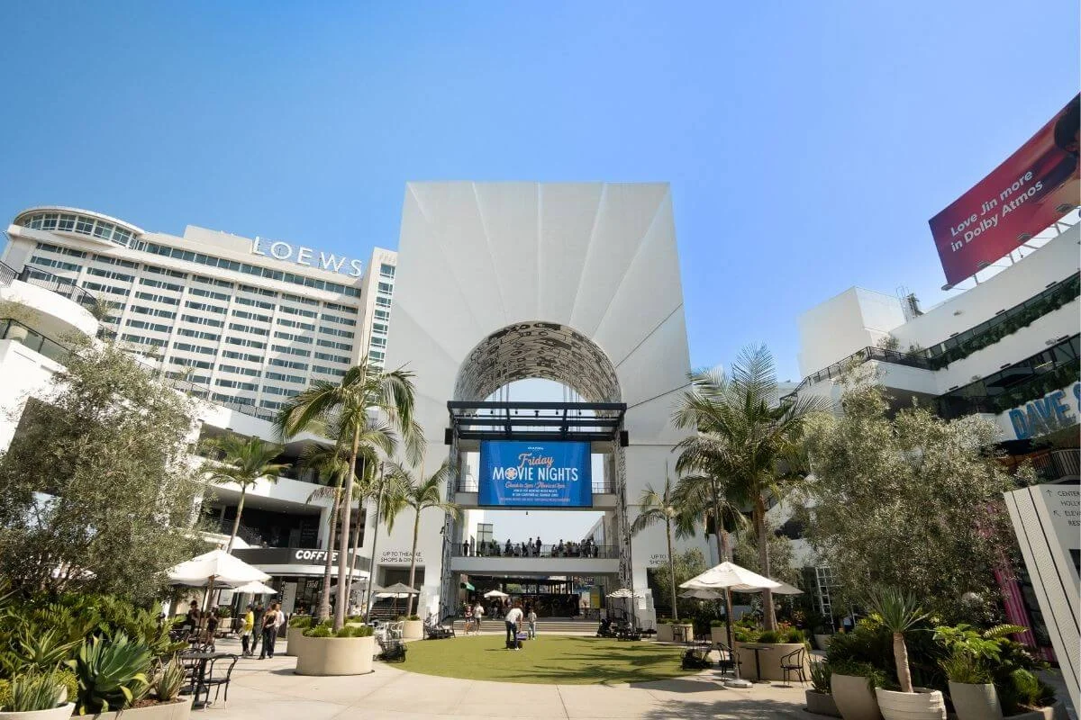 Open-air courtyard at Hollywood & Highland Center with palm trees, shops, and visitors near the entrance to Hollywood attractions in Los Angeles.
