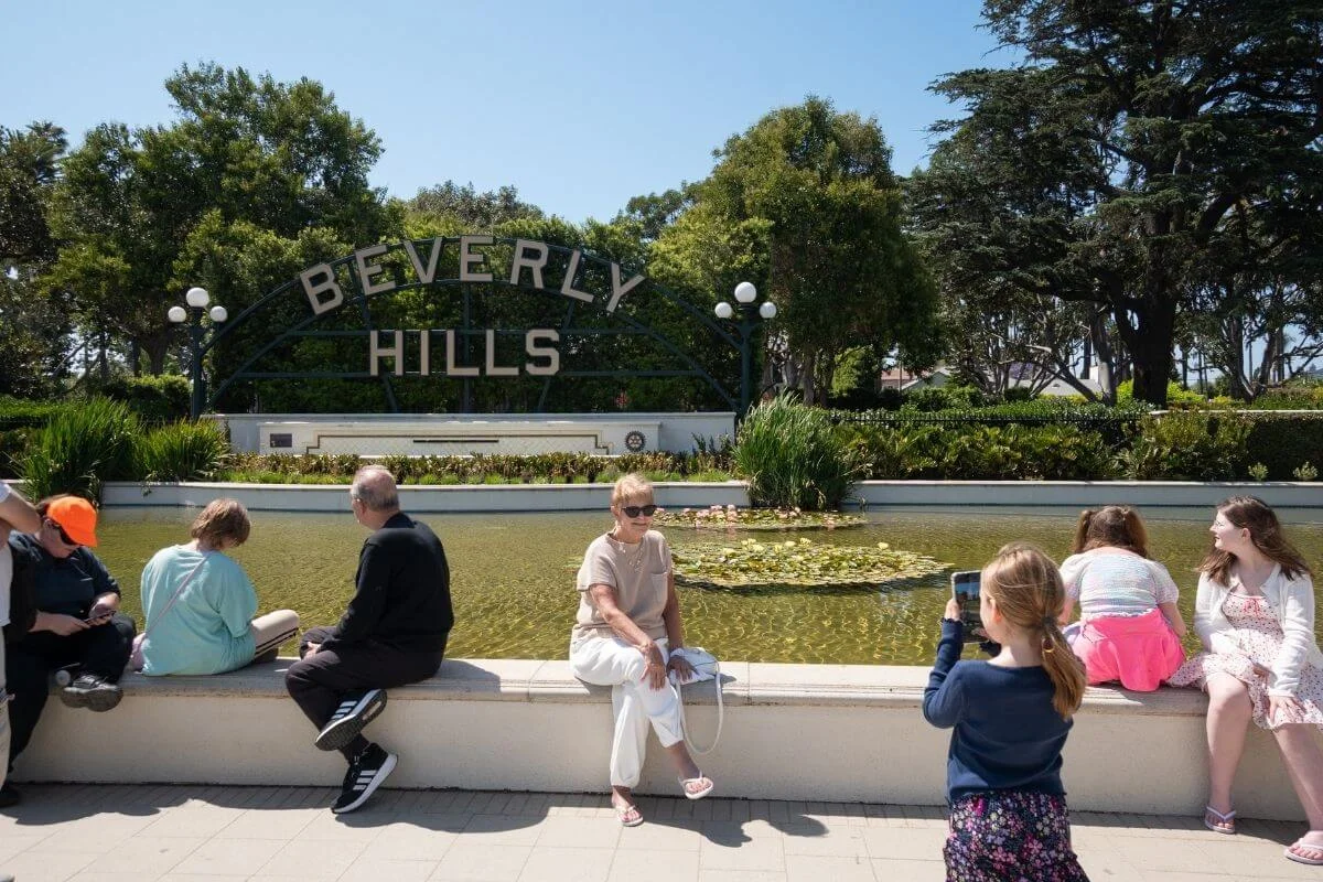 Tourists relaxing and taking photos in front of the Beverly Hills sign and lily pond in Beverly Gardens Park, Los Angeles.