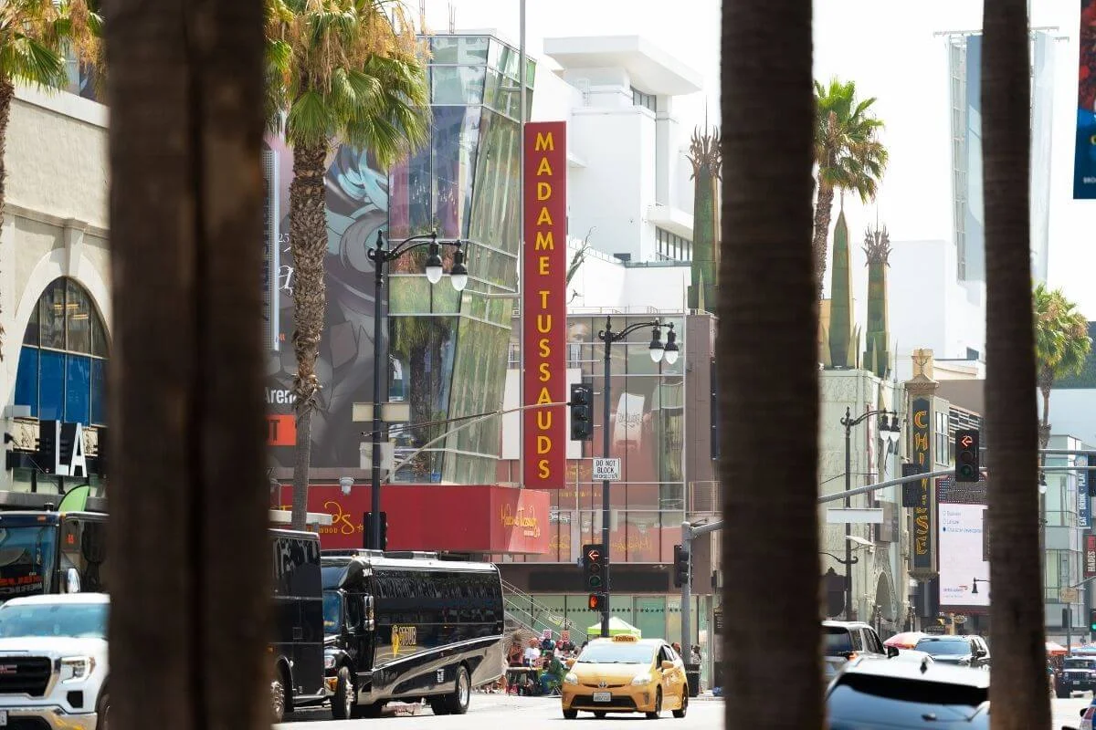 Street view of Hollywood Boulevard featuring Madame Tussauds museum sign, palm trees, and traffic in Los Angeles.