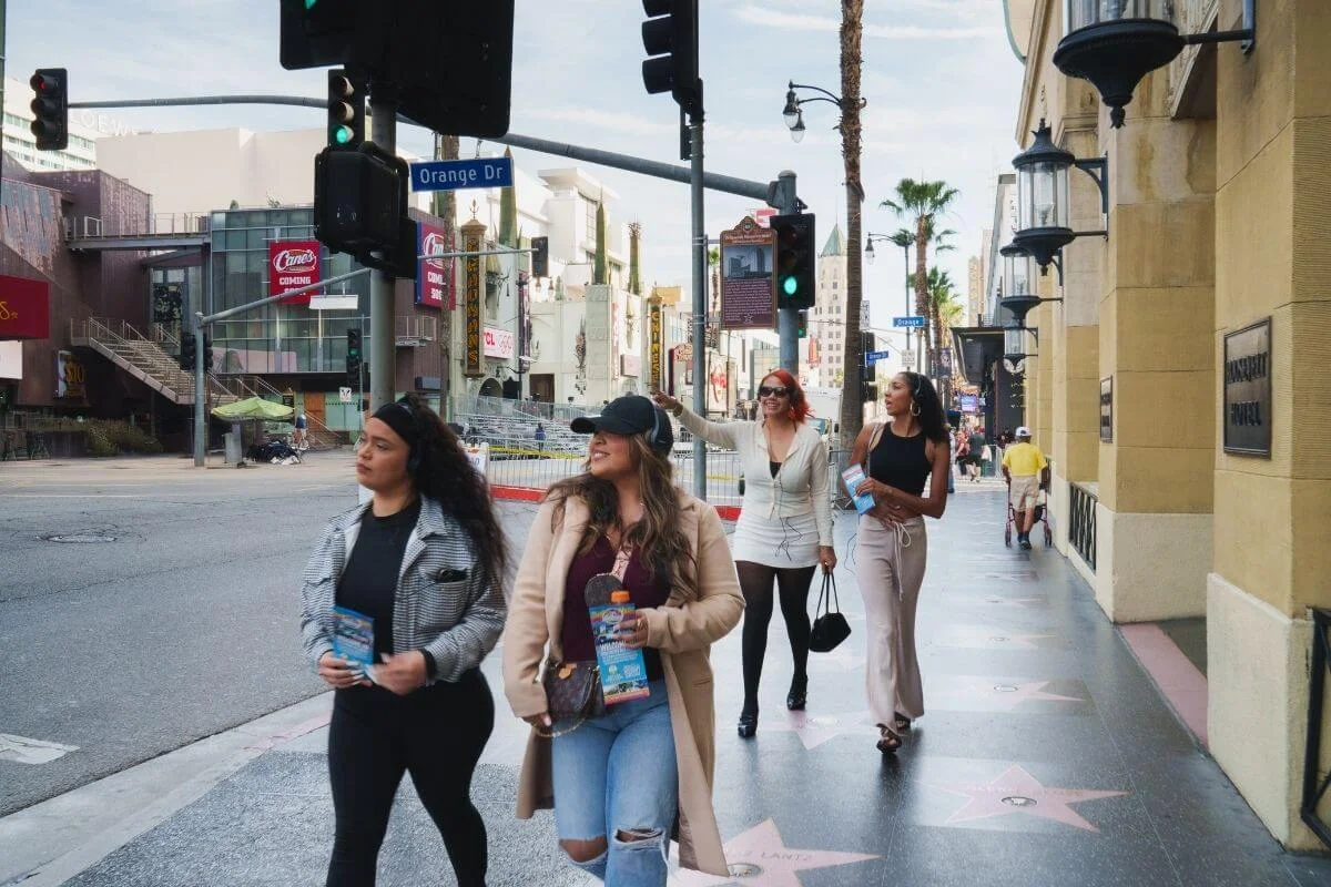 Group of tourists walking along the Hollywood Walk of Fame near Orange Drive, exploring Los Angeles landmarks on a sightseeing tour.