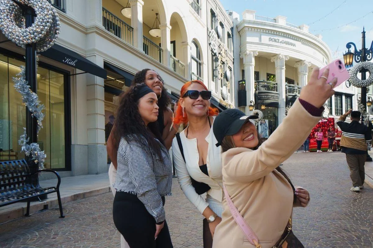 Group of friends smiling and taking a selfie on Rodeo Drive in Beverly Hills, surrounded by luxury shops and festive street decorations.