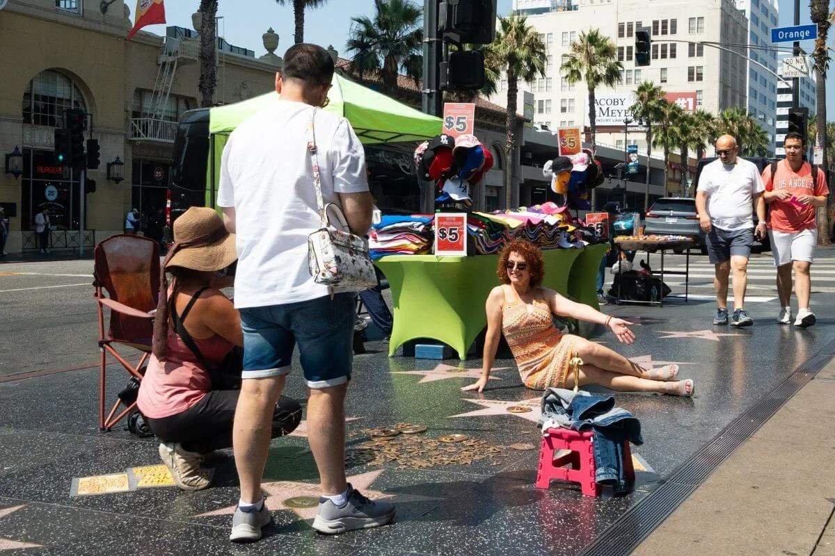 Visitors posing for photos on the Hollywood Walk of Fame near street vendors and souvenir stands in Los Angeles.