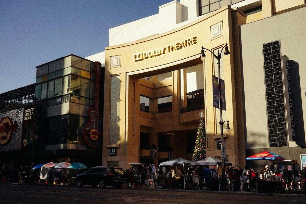 Exterior of the Dolby Theatre at Ovation Hollywood in Los Angeles with visitors gathered outside near shops and street vendors.