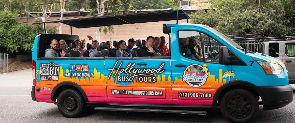 Colorful Hollywood Bus Tours van with passengers waving during a guided city tour in Los Angeles, showcasing an open-air sightseeing experience.