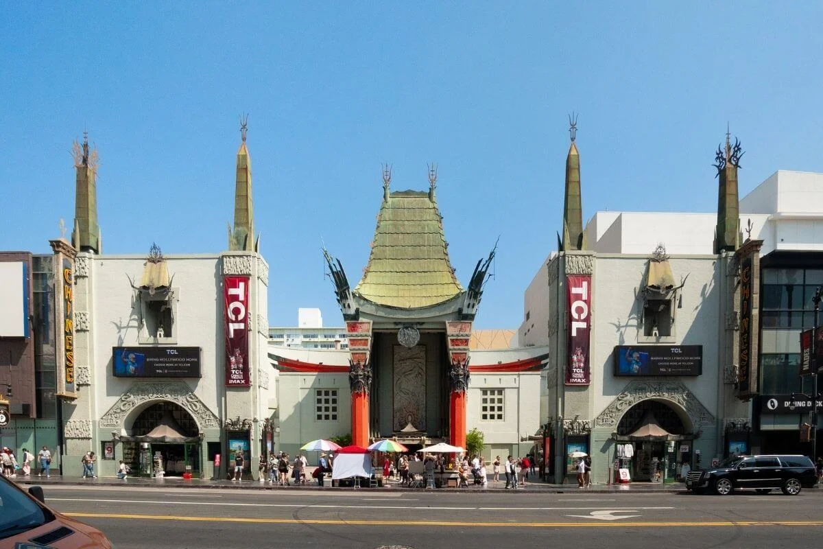 Front facade of TCL Chinese Theatre on Hollywood Boulevard in Los Angeles, featuring its iconic pagoda-style roof, ornate red columns, and TCL IMAX banners with tourists gathered out front.
