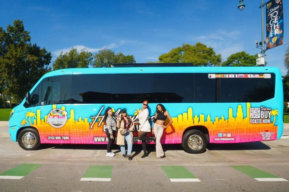Group of travelers posing in front of a colorful Hollywood Bus Tours vehicle during a sightseeing tour in Los Angeles.