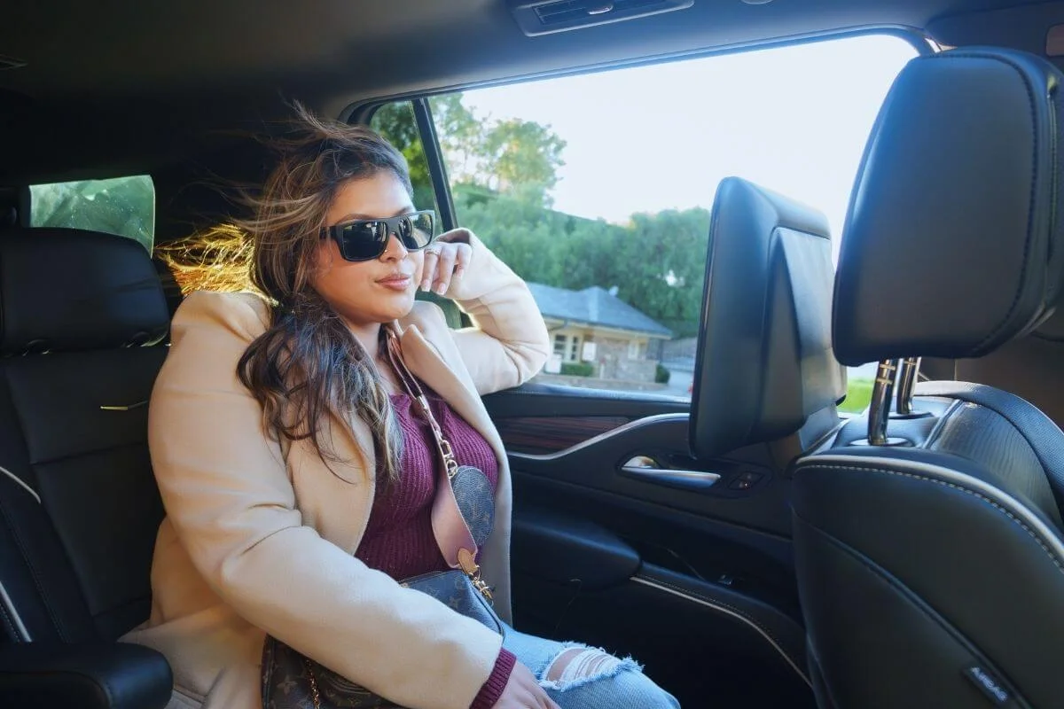 A woman wearing sunglasses relaxing in the back seat of a vehicle while touring through Los Angeles during daylight.