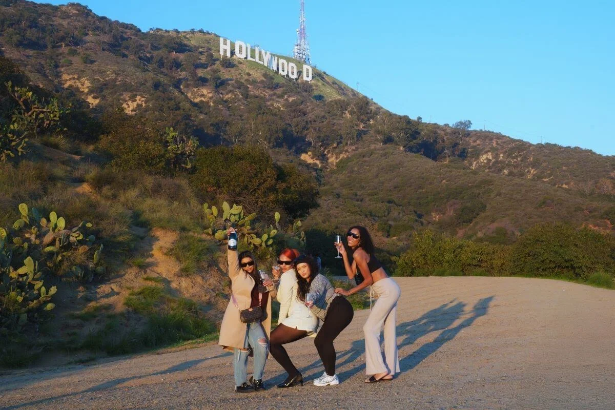 A group of travelers posing with drinks near the iconic Hollywood Sign during a sightseeing tour in Los Angeles.