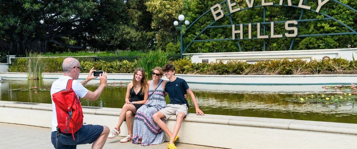 A family posing for a photo in front of the iconic Beverly Hills sign and reflecting pool during a sunny day in Los Angeles.