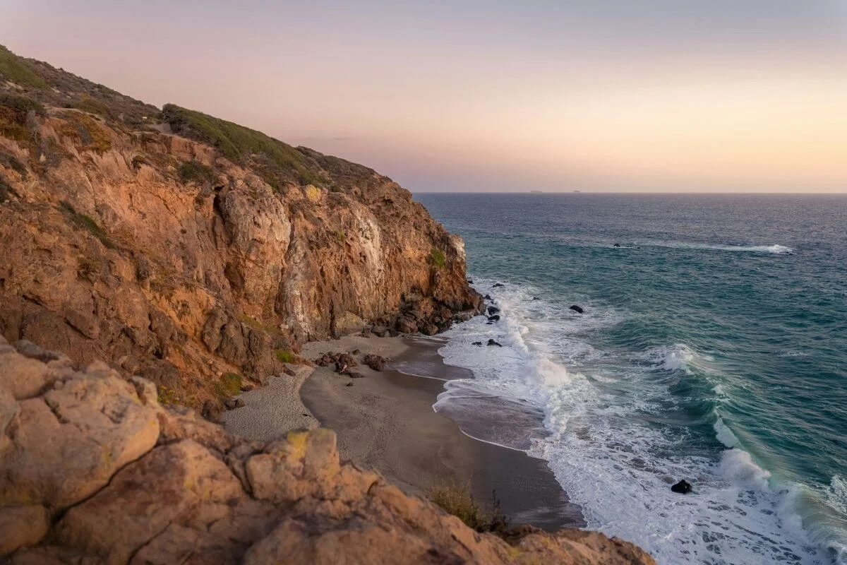 Rocky Malibu cliffside overlooking ocean waves at sunset