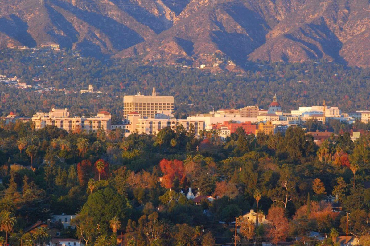 Aerial view of Pasadena city buildings nestled among autumn trees with mountain backdrop at sunset