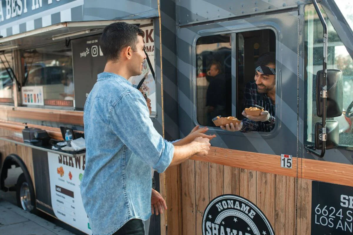 Man receiving a food order from a vendor at a shawarma food truck on a Los Angeles street