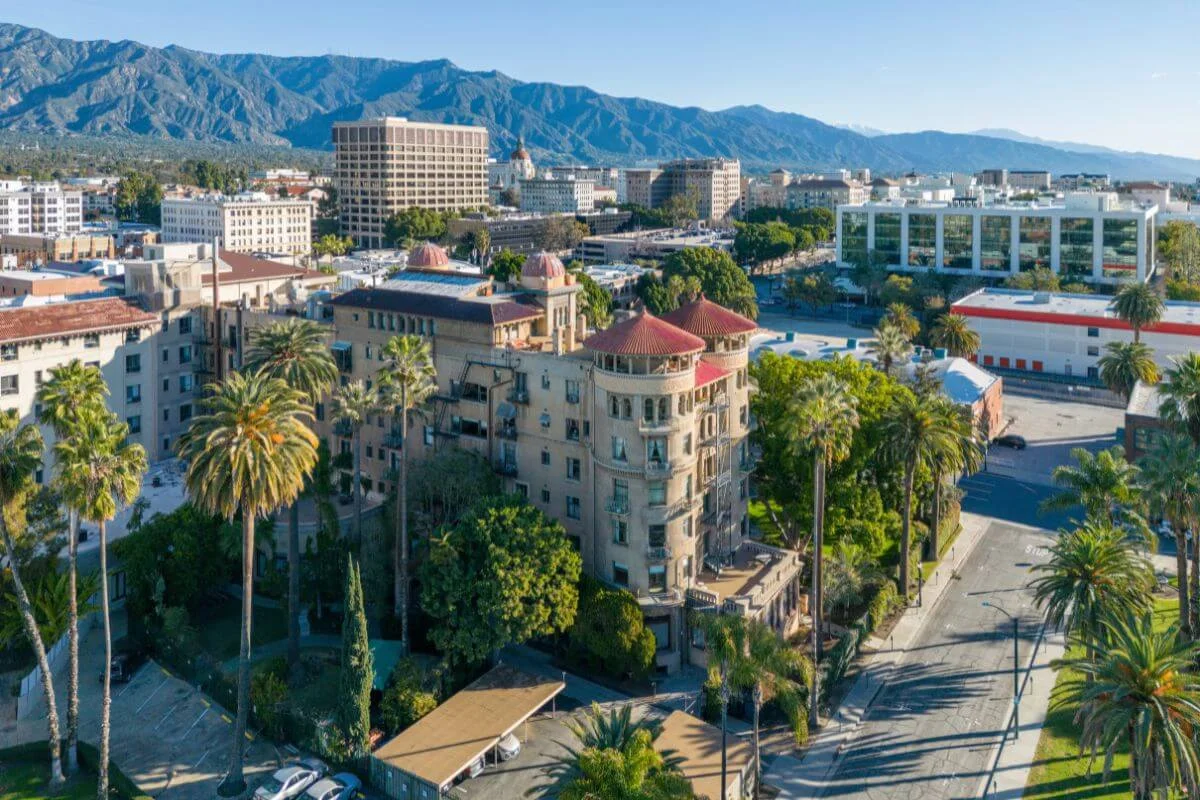 Drone view of ornate historic building with red domed towers surrounded by palm trees and mountain range