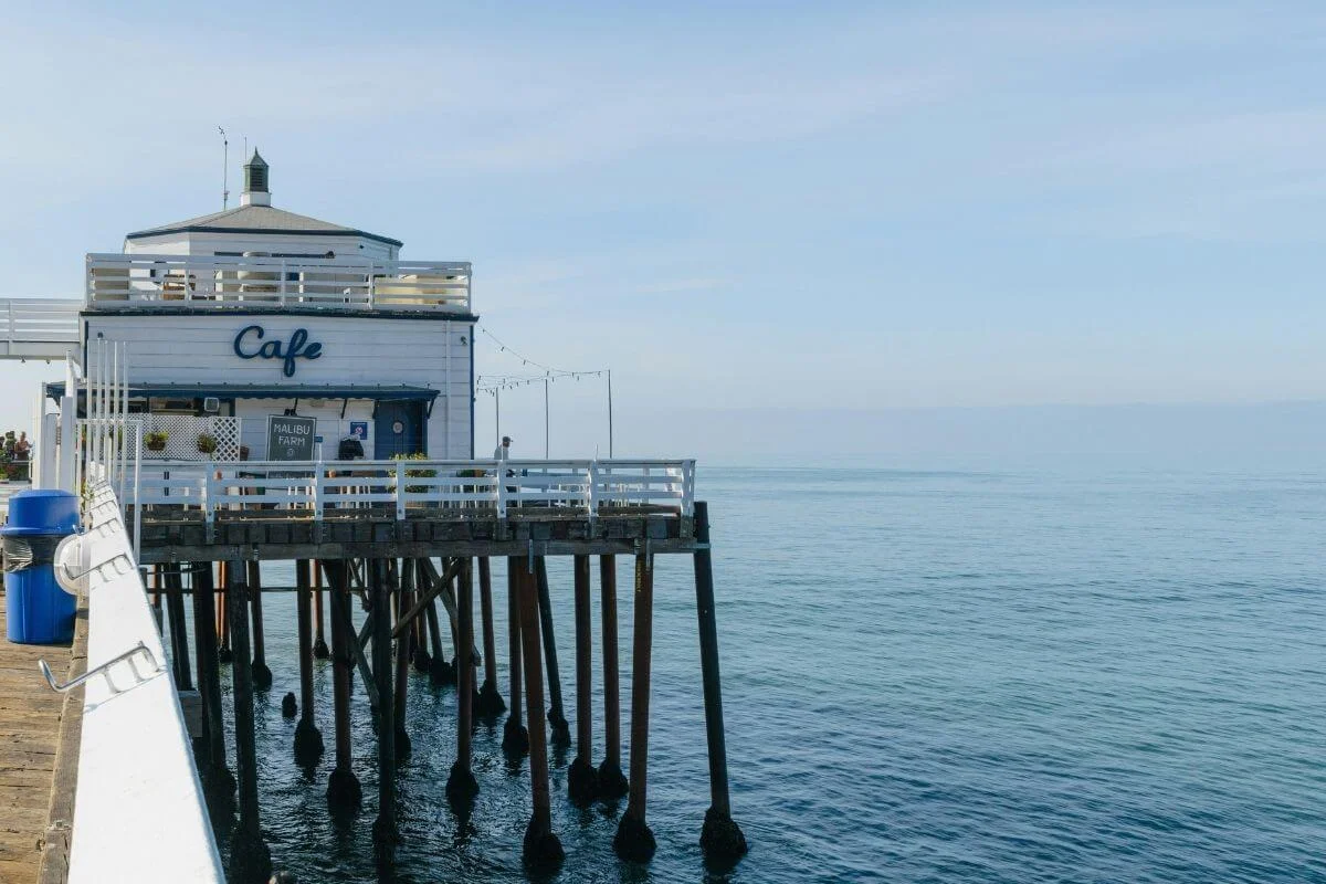 White Malibu Farm Cafe building sitting on pier stilts over calm blue ocean water